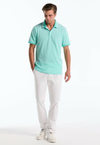 Polo shirt vert menthe à manches courtes et col, avec de fines rayures blanches. Associé à un pantalon blanc et des baskets claires.