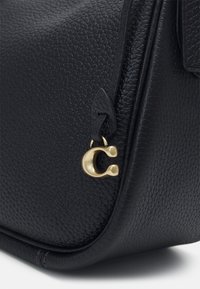 Czarna torebka skórzana z fakturowanej skóry o gładkim wykończeniu, z elementami z metalu w kolorze złotym oraz charakterystycznym zawieszką z logo.