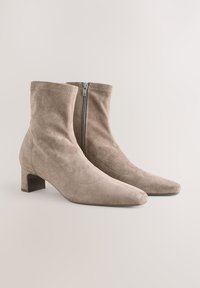 Beige suede ankle boots with a pointed toe, short block heel, and a zip fastening on the side. Smooth texture, minimal stitching detail.