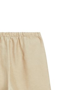 Tissu beige avec ceinture élastique froncée, texture lisse et coutures verticales subtiles visibles sur un fond clair.