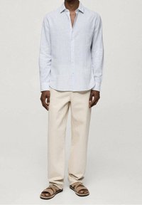 Jasnoniebieska, w paski, koszula z długim rękawem, zapięta na guziki, połączona z beżowymi, lnianymi spodniami i brązowymi sandałami. Koszula ma standardowy kołnierzyk i luźny krój.