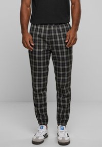 Schwarz-weiß-karierte Hose mit elastischem Bund und schmal zulaufendem Bein. Getragen mit weißen und grauen Sneakers, die das Karomuster betonen.