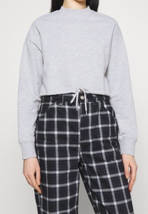 Light grey sweatshirt with a high neck and drawstring detail, paired with black and white plaid pants featuring a relaxed fit and pockets.