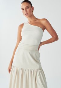 Jasno-beżowy, ribbed top na jedno ramię w połączeniu z kremową plisowaną spódnicą. Lekki, teksturowany materiał z detalem w postaci ściągnięcia w talii.