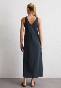 Robe maxi sans manches gris foncé avec un dos en V, fabriquée à partir d'un tissu lisse, présentant un design fluide et une silhouette minimaliste.