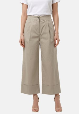 Donna che indossa pantaloni beige a gamba larga a vita alta con orli risvoltati e un top bianco a maniche corte, abbinati a tacchi nudi con cinturino alla caviglia.