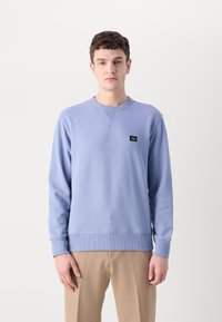 Lyseblå sweatshirt lavet af bomuld, med rund halsudskæring, ribbede manchetter og et lille logo-plaster på brystet. Glat tekstur.