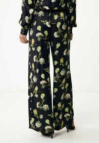 Luźne czarne spodnie z botanicznym nadrukiem przedstawiającym zielone gruszki i białe kwiaty. Wykonane z gładkiego materiału, o szerokich nogawkach i subtelnym połysku.