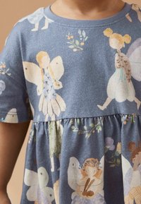 Modrá bavlněná šaty s fantazijními vzory víl a květin, krátké rukávy, nařasený pás a měkká textura.