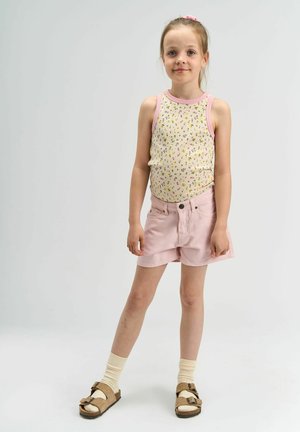 Farkatut t-paita, jossa on vaaleanpunaiset reunat, yhdistettynä vaaleanpunaisiin shortsit. Mallilla on päällään beiget sandaalit ja vaaleancreme-sukat.