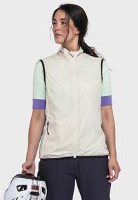 Leichte, cremefarbene Weste mit hohem Kragen, schwarzem Besatz und Reißverschlusstaschen, kombiniert mit einem mintfarbenen Shirt und lila Ärmeln, gehalten von einer Person.
