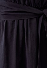 Zwarte stoffen jurk met een gesmokte taille, een gestrikt lint en vloeiende plooien, die een zachte textuur met een matte afwerking presenteert.