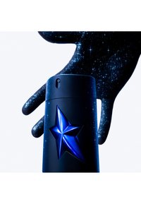 Bouteille de parfum cylindrique noire avec un motif étoilé bleu en relief, tenue par une main recouverte d'un motif cosmique étoilé.