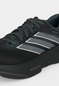 Μαύρο παπούτσι για τρέξιμο με γκρι και λευκές ρίγες, μαλακό πάτο με την ένδειξη "DREAMSTRIKE+" και το κείμενο "SUPERNOVA" στο πλάι.