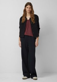 Zwarte jas met twee voorzakken, bordeauxrode v-hals top en losse zwarte broeken met een gladde textuur, gecombineerd met beige instappers.