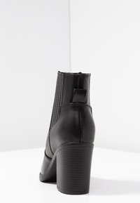 Bottine en cuir noir avec côtés côtelés, bout rond et talon bloc texturé. Équipée d'une languette à l'arrière pour un enfilage facile.