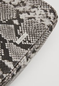 Pochette texturée façon peau de serpent en noir et blanc, avec une surface lisse et un accent logo argenté. Forme rectangulaire compacte.