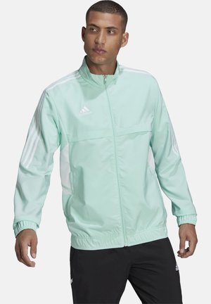 Licht mintgroene jas met een hoge kraag, volledige rits en elastische boorden. Bevat witte zijpanelen en drie witte strepen op de mouwen.