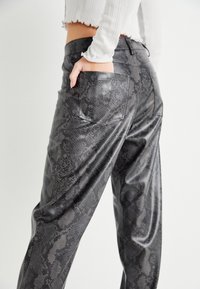 Schwarze Kunstlederhosen mit Schlangenhautmuster, ausgestattet mit Gesäßtaschen und einem lässigen Schnitt. Die Textur wirkt glatt und glänzend.
