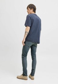 Marinblå bomullströja med avspänt snitt, korta ärmar och rundad halsringning, i kombination med mörka jeans och beige skor.