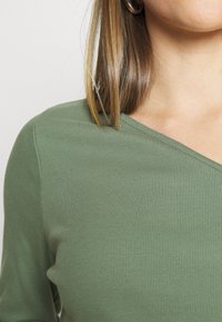 Fitted ribbed top in olive green with a v-neckline. The fabric texture appears soft and stretchy, highlighting the structured design.