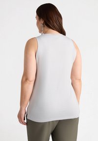 Vaaleanharmaa hihaton paita, jossa on pyöreä kaula-aukko, sileä pinta ja sivurei'ät, yhdistettynä oliivinvihreisiin pantsuihin, nähtynä takaa.