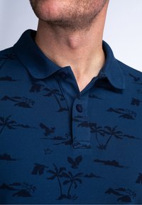 Mörkblå pikétröja med en strukturerad design som visar mörka mönster av palmer och fåglar, knäppt krage och korta ärmar.