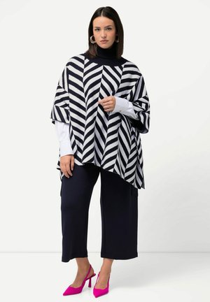 Poncho rayé noir et blanc avec un col montant, porté sur une chemise blanche, associé à des culottes marina et des escarpins roses.