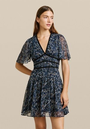 Abito corto blu navy con maniche corte trasparenti, scollatura a V profonda e motivo floreale in bianco e azzurro chiaro. Gonna svasata con vita arricciata.