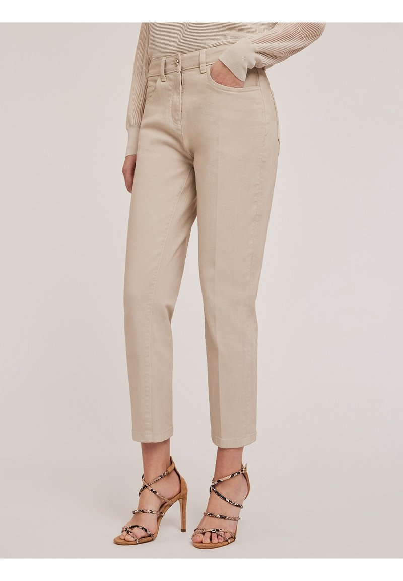 Pantalons en coton beige avec une taille ajustée, des jambes droites et des poignets retroussés. Portés avec des sandales à talons hauts beige à lanières.