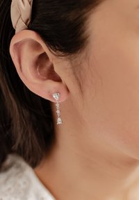 Pendientes de plata con una parte superior en forma triangular y un colgante en forma de gota, adornados con pequeñas piedras transparentes a lo largo de la cadena.