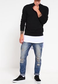 Pull noir à encolure ronde, jean déchiré bleu clair à coupe décontractée, et baskets noires avec semelles blanches.