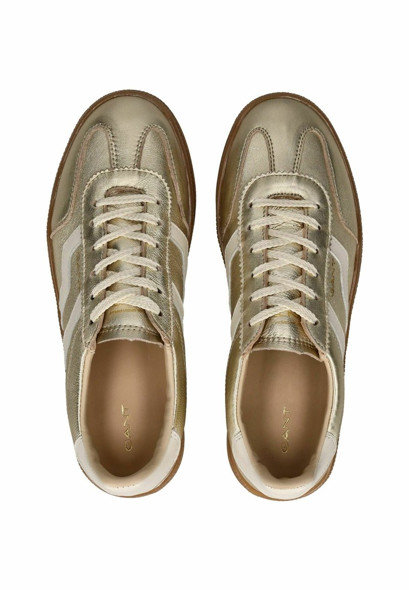 Baskets dorées métalliques avec une tige en cuir lisse, des rayures blanches sur les côtés, un bout arrondi et des lacets plats, le tout reposant sur une semelle en caoutchouc.