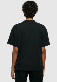 T-shirt en coton noir avec une coupe décontractée, des manches courtes et un col rond. Texture lisse et sans motifs ni accents visibles.