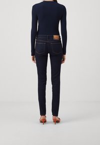 Mörkblå denimjeans med smal passform, med bakfickor och kontrasterande sömmar. Kombinerat med en figurnära marinblå topp och sandaler med öppen tå.