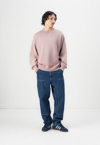 Rosa fleece genser med rund hals, avslappet passform, kombinert med løse blå denim jeans med lommepatcher, brukt med mørkeblå sneakers.
