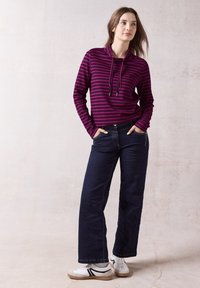 Top a maniche lunghe, bordeaux e blu a righe con collo a cappuccio e lacci, abbinato a pantaloni wide-leg in denim scuro e sneakers bianche.
