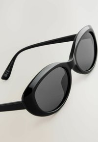 Lunettes de soleil noires surdimensionnées avec une forme audacieuse en papillon, présentant des montures lisses et brillantes ainsi que des verres foncés. Fines branches droites.