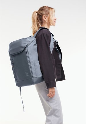 Sac à dos gris fabriqué à partir de matériau durable, avec une poche avant zippée, des bretelles ajustables et un design épuré et moderne.