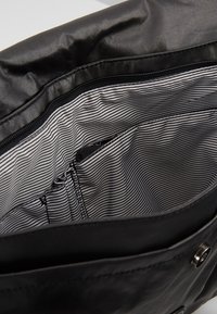 Intérieur d'un sac en tissu noir avec une texture lisse, doté d'une doublure rayée et d'une poche zippée. Comprend des compartiments pour l'organisation.