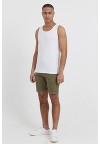 Weißes Baumwoll-Tanktop, olivgrüne Shorts mit umgeschlagenen Säumen und weiße Sneakers. Das Modell steht aufrecht mit entspannten Armen an den Seiten.