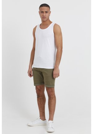 Débardeur en coton blanc, shorts vert olive avec des poignets roulés, et baskets blanches. La modèle se tient droite avec les bras relaxés de chaque côté.