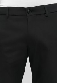 Zwarte broek van gladde stof, met een knoopsluiting, een vlakke voorkant en een standaard zakontwerp. Minimalistische stijl met een op maat gemaakte pasvorm.