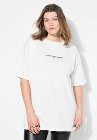 Camiseta blanca de gran tamaño hecha de algodón, con mangas cortas, que presenta el texto negro "CELEBRATE WITH LEMONADE" y un pequeño detalle gráfico.
