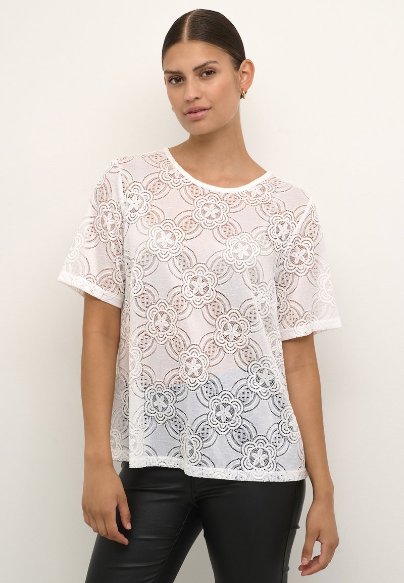 Weißes Spitzen-T-Shirt mit Blumenmustern, kurzen Ärmeln und einem runden Ausschnitt, über einem Oberteil in einfarbigem Design getragen. Glatte Textur und lockere Passform.