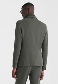 Blazer entallado verde oliva con cuello con muesca, cierre de un solo botón y detalle de puño con cuatro botones. Tejido suave y estructurado.