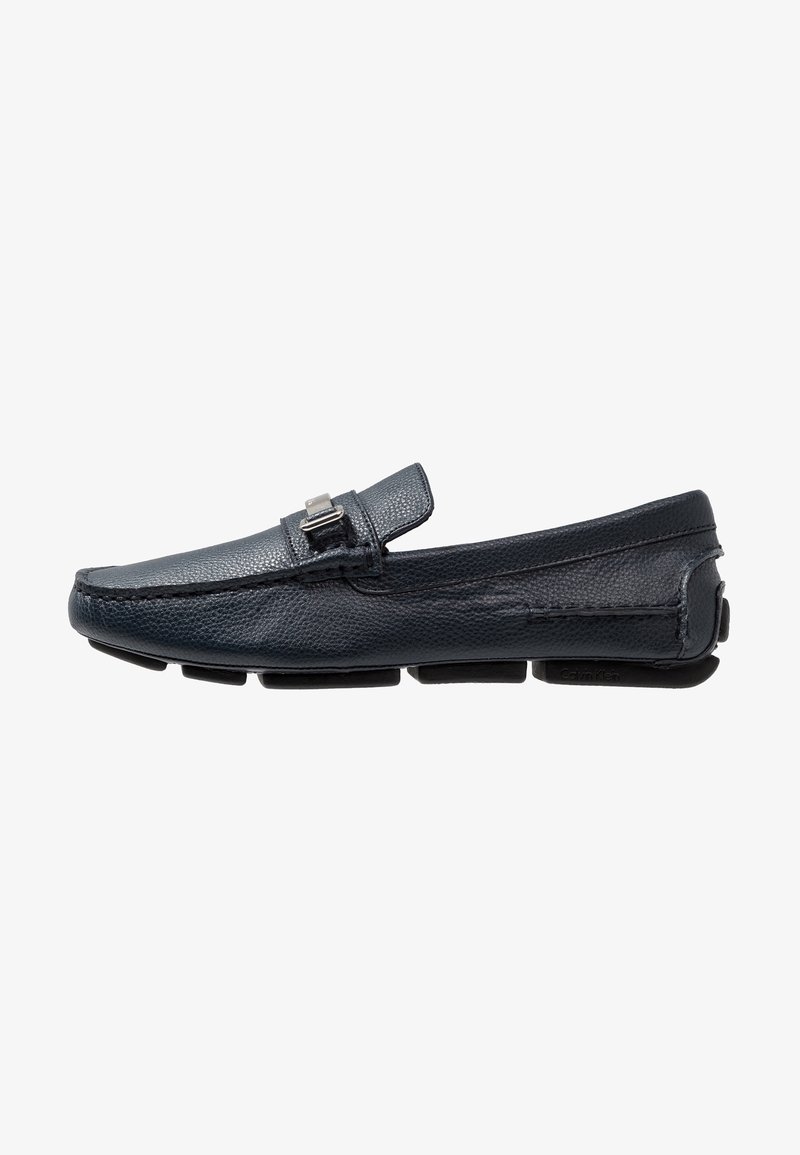 Mocassin en cuir bleu foncé à finition texturée, orné d'une boucle en métal argenté, et doté d'une semelle en caoutchouc noir flexible. Forme élégante avec des détails cousus.
