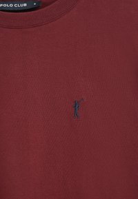 Bordeaux sweatshirt met een ronde hals en geribbelde afwerking, met een kleine zwarte geborduurde figuur die een stok vasthoudt aan de voorkant.