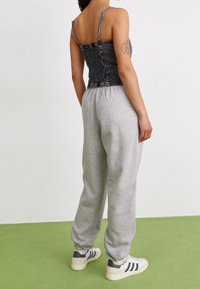 Svart jeanscorsettopp med justerbara axelremmar, tillsammans med grå sweatpants. Båda plaggen har en avslappnad passform. Vita sneakers med svarta ränder.