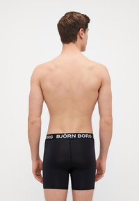 Μαύρες αθλητικές σλιπ με λεία υφή, ελαστική μέση που φέρει το λογότυπο "BJÖRN BORG" σε λευκή γραφή. Όψη από πίσω, μινιμαλιστικός σχεδιασμός.